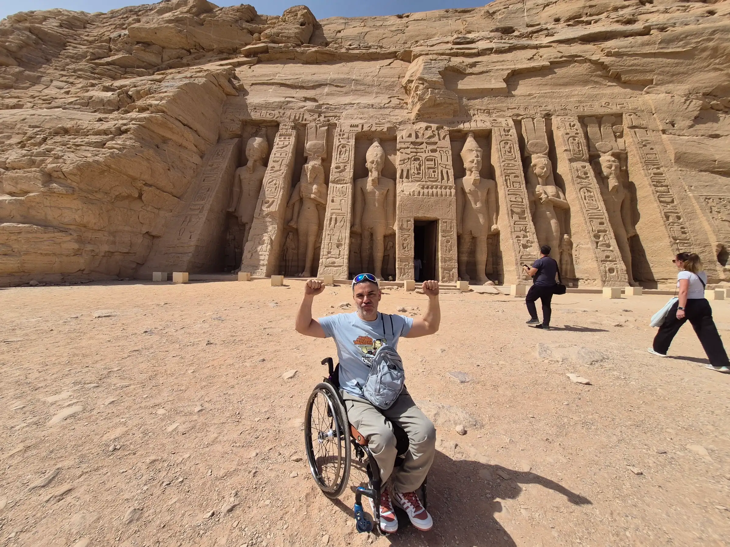 Un viajero en silla de ruedas levanta los brazos, feliz, frente al templo de Abu Simbel, en Egipto.